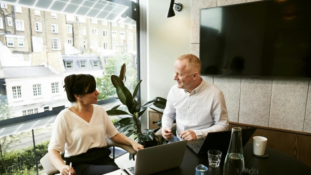 Home Dua profesional bisnis sedang mengadakan rapat tim di kantor modern di London Membahas cara menghitung pajak, cara menghitung keuntungan.